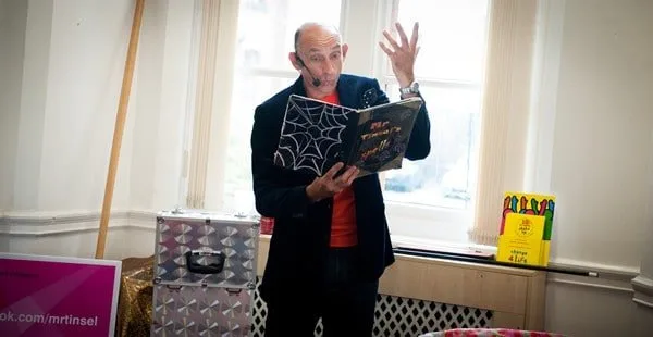 Mr Tinsel raising a hand while performing in a room