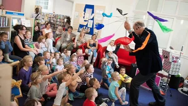 Children and parents sitting on the floor watching Mr Tinsel perform